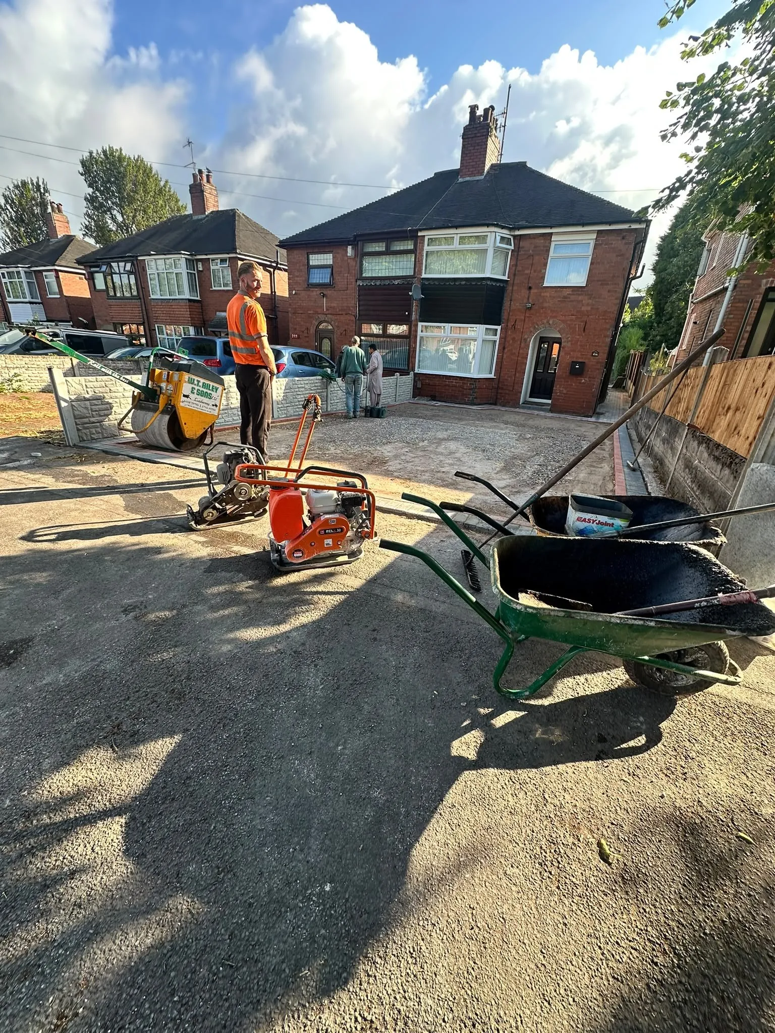 Workers laying a new tarmac driveway with a roller and a wheelbarrow