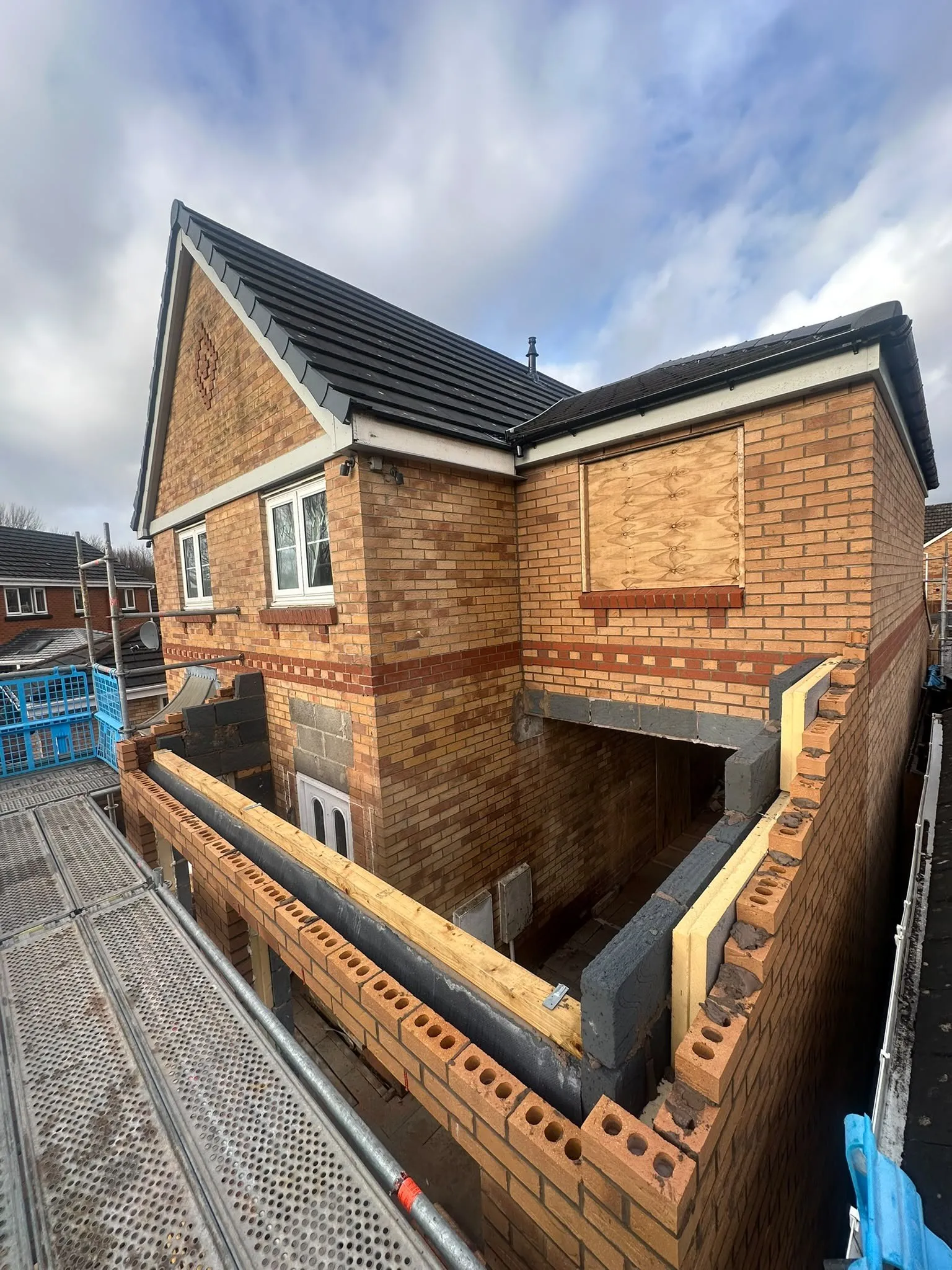 New brick side extension going up beside a house, seen from scaffolding