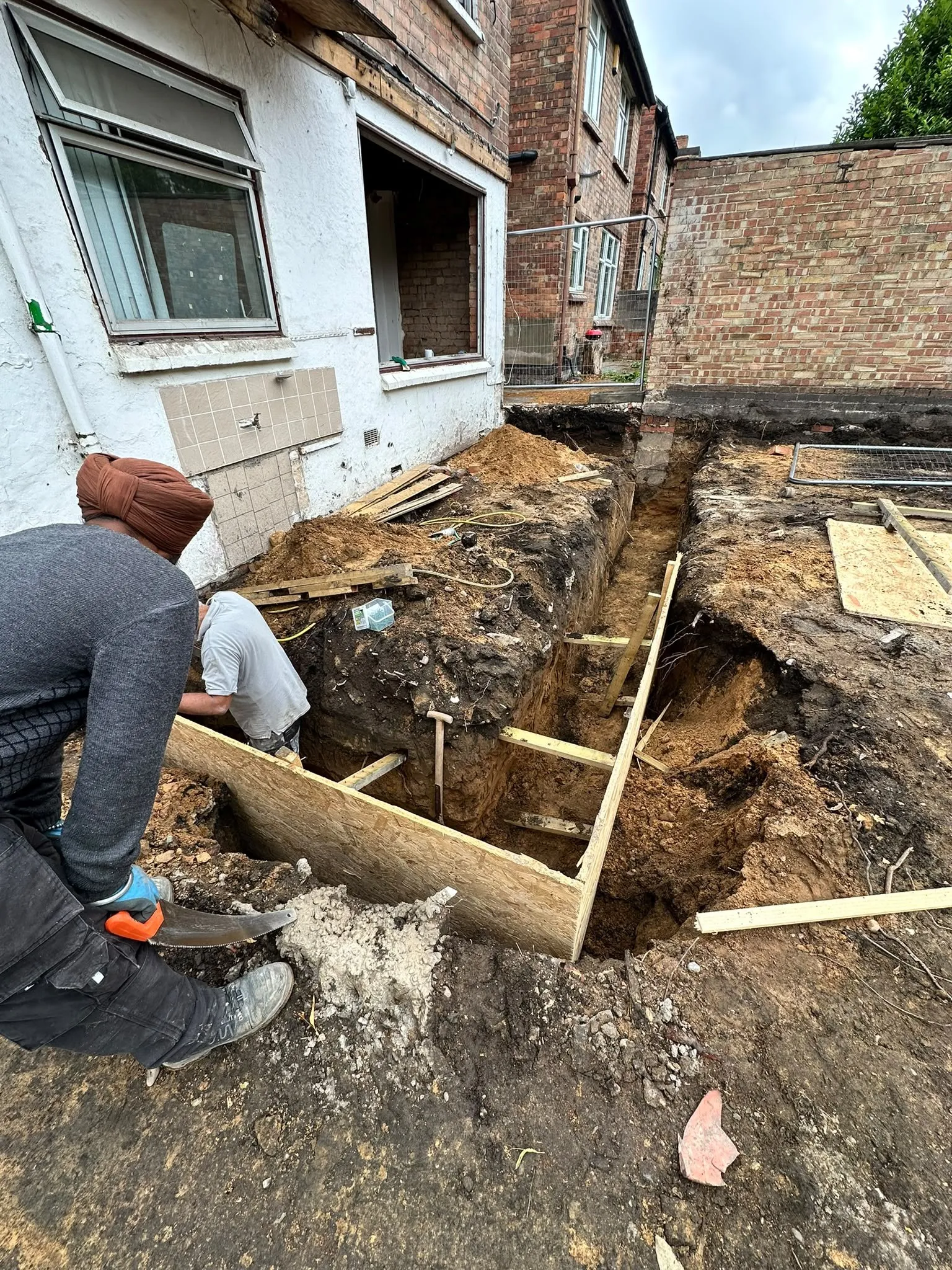 Before: Workers digging foundation trenches at the back of a rendered house