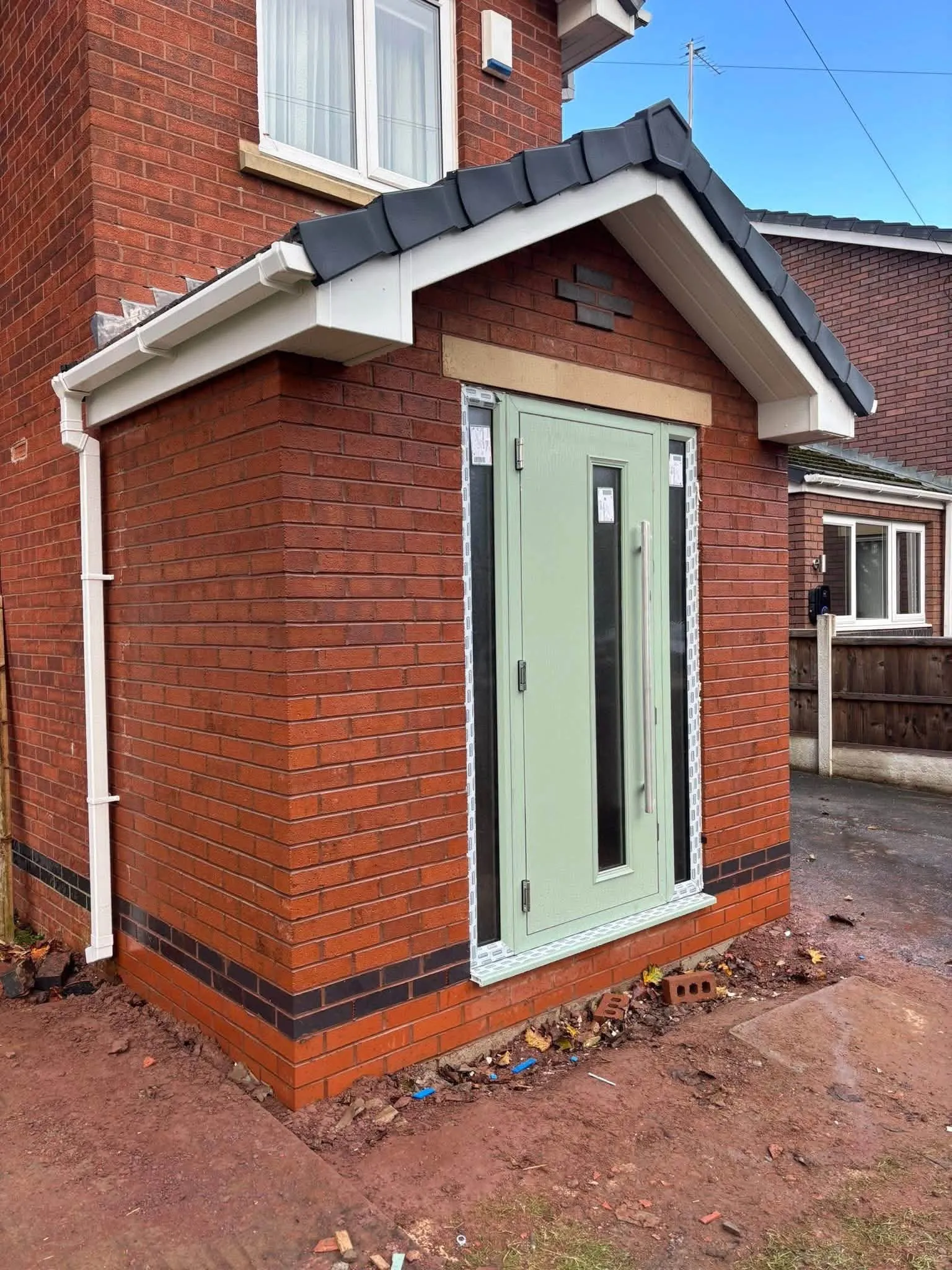 New brick porch with a tiled roof and a sage green front door