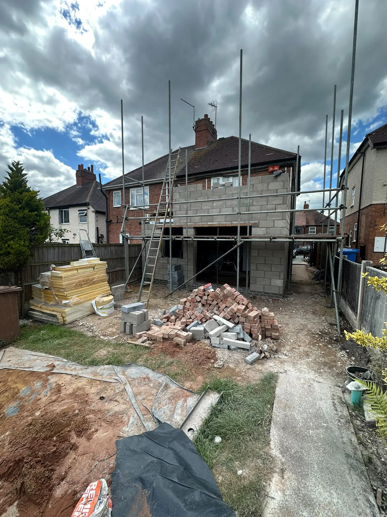 Two-storey extension in grey blockwork with scaffolding, seen from the garden