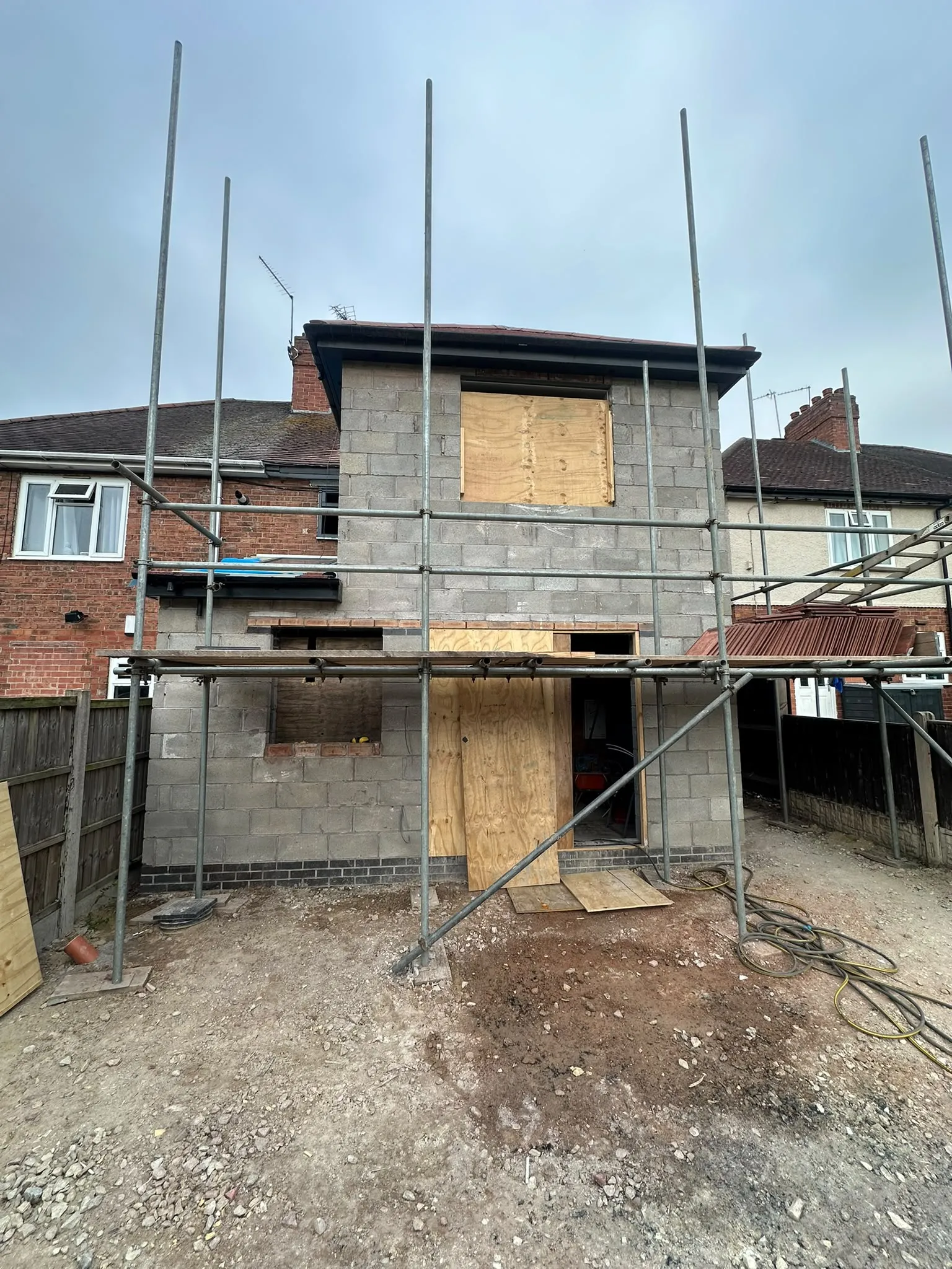 Shell of a two-storey rear extension with boarded openings and scaffolding