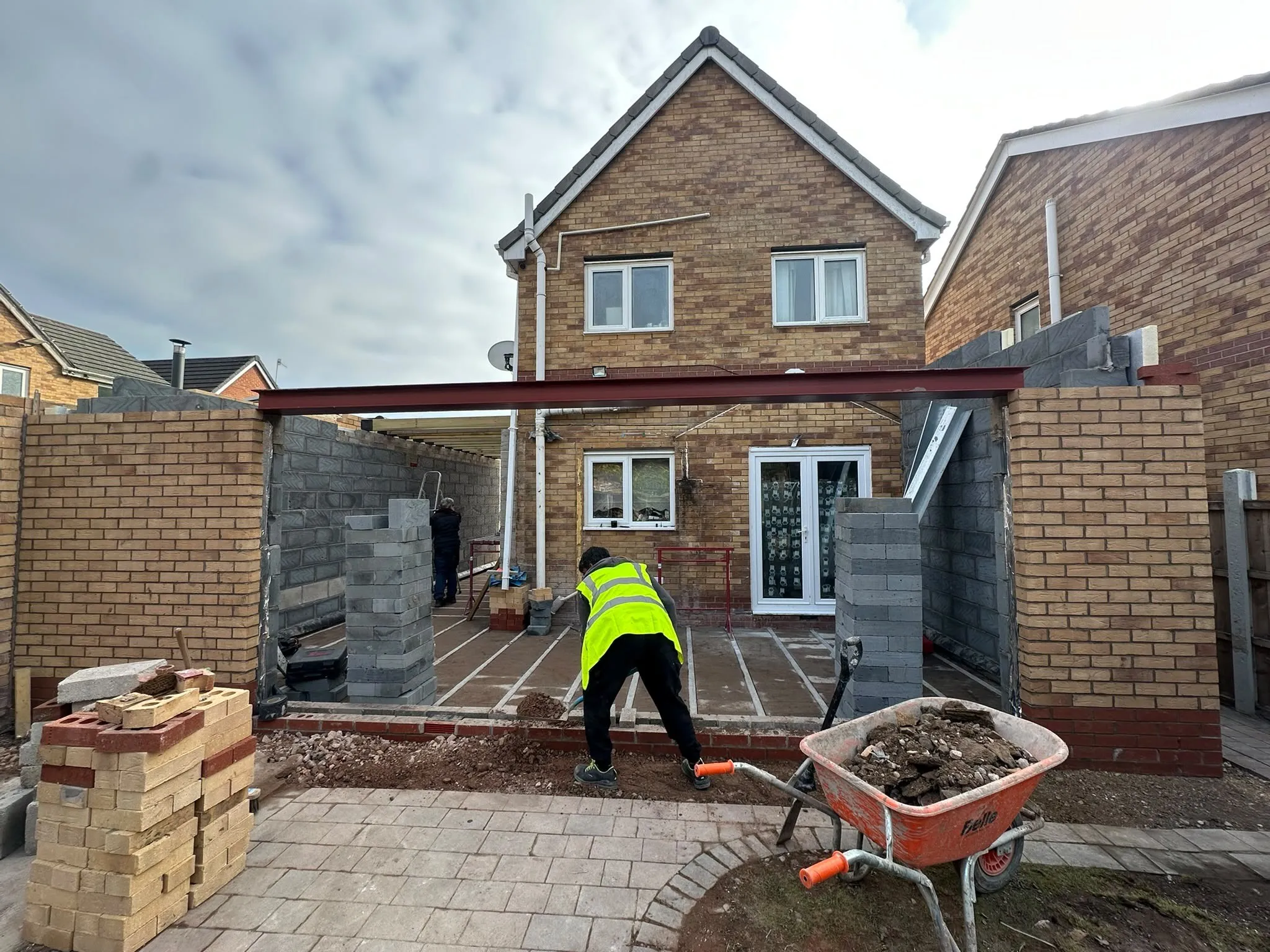 Worker building blockwork walls under a new steel beam at the back of a house