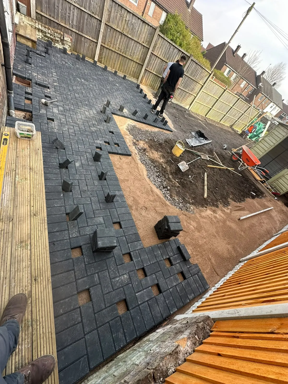 Grey block paving being laid across a back garden