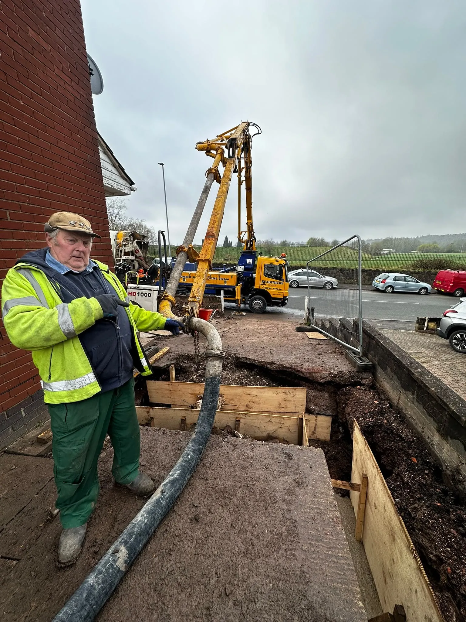 Worker guiding a concrete pump hose into foundation formwork