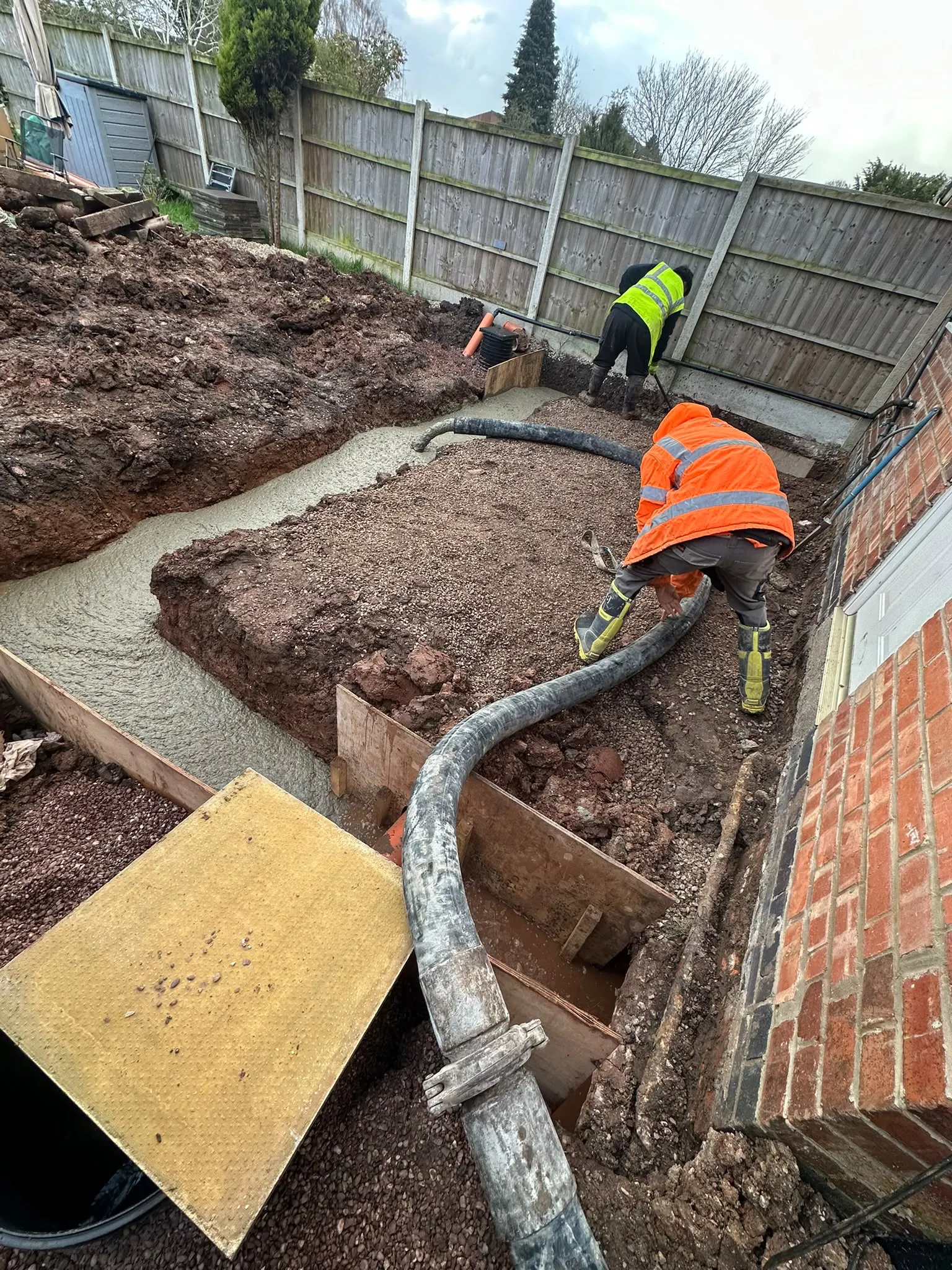 Workers pouring concrete into foundation trenches with a pump hose