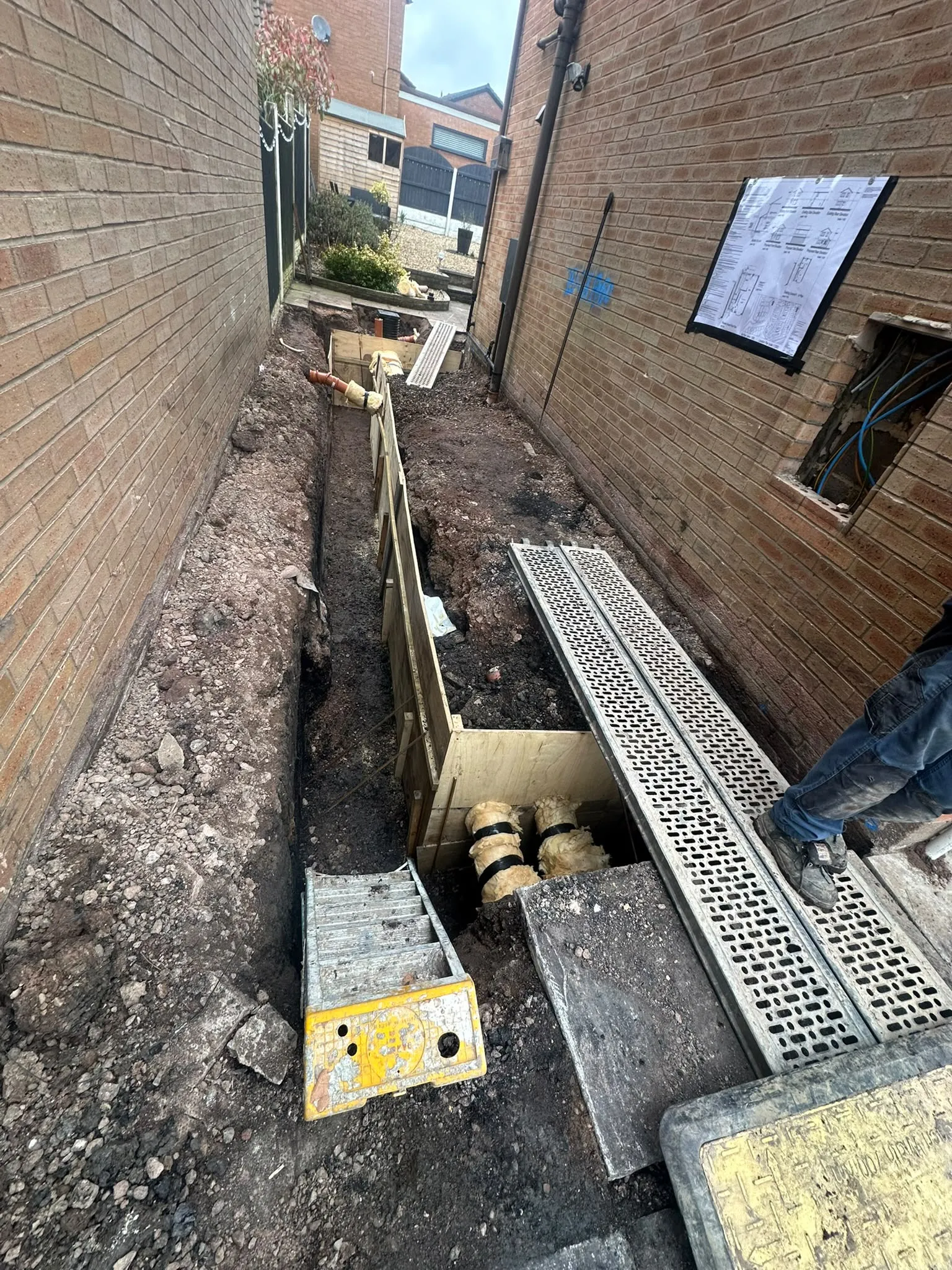 Trench with support panels dug between two houses