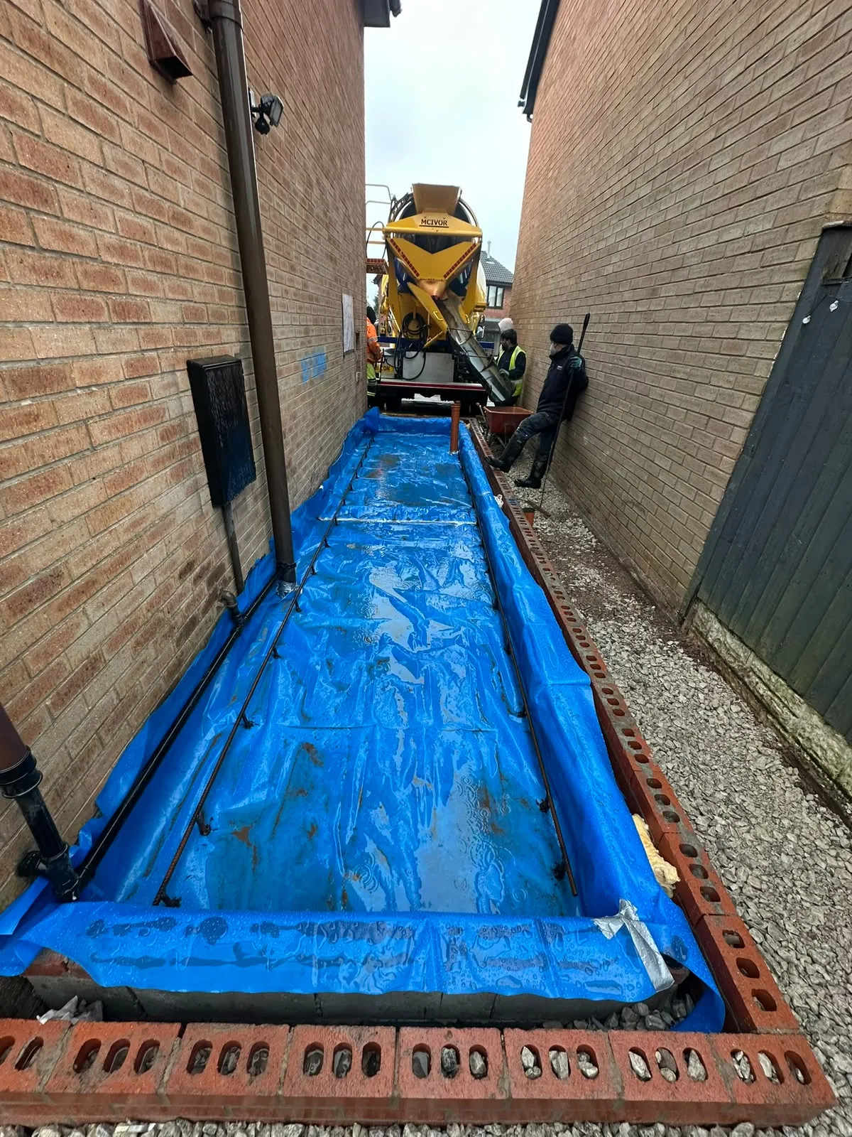 Narrow strip beside a house lined with blue sheeting, ready for concrete