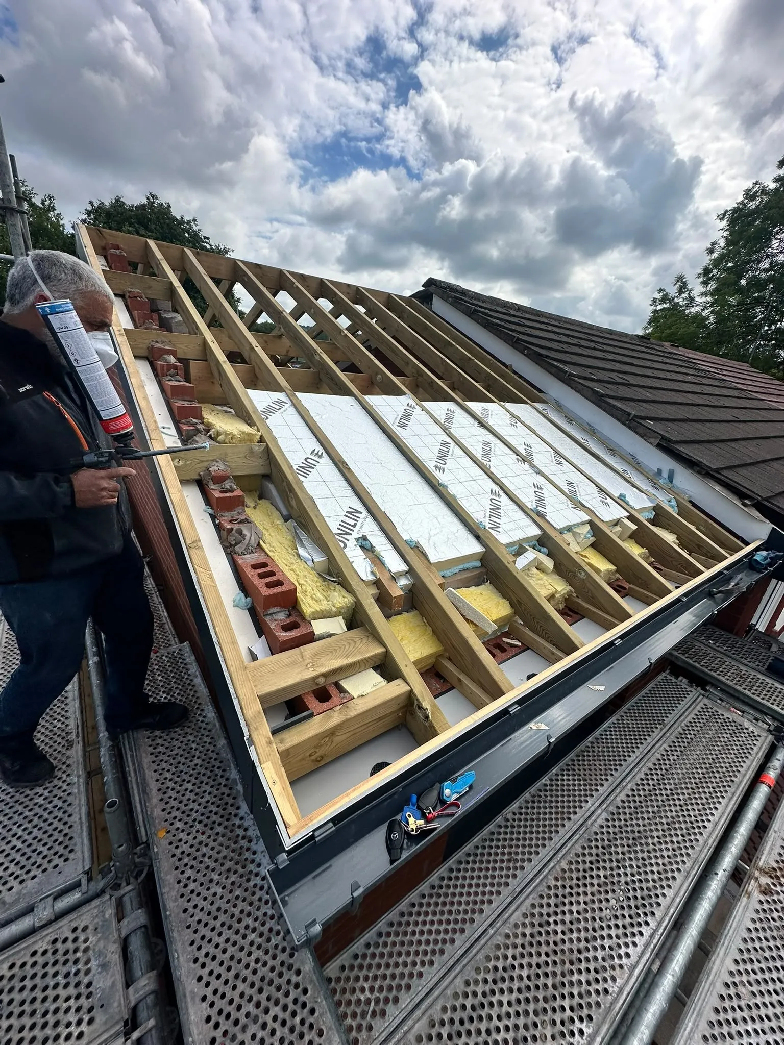 Worker sealing insulation boards between roof timbers