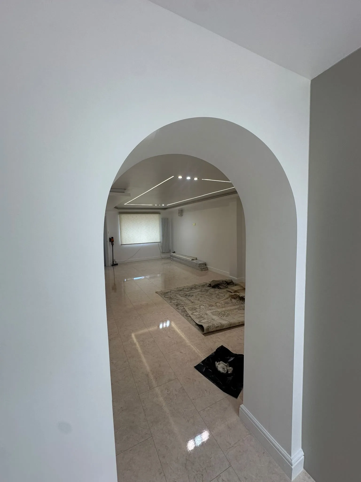Smooth white arched doorway into a room with a glossy tiled floor