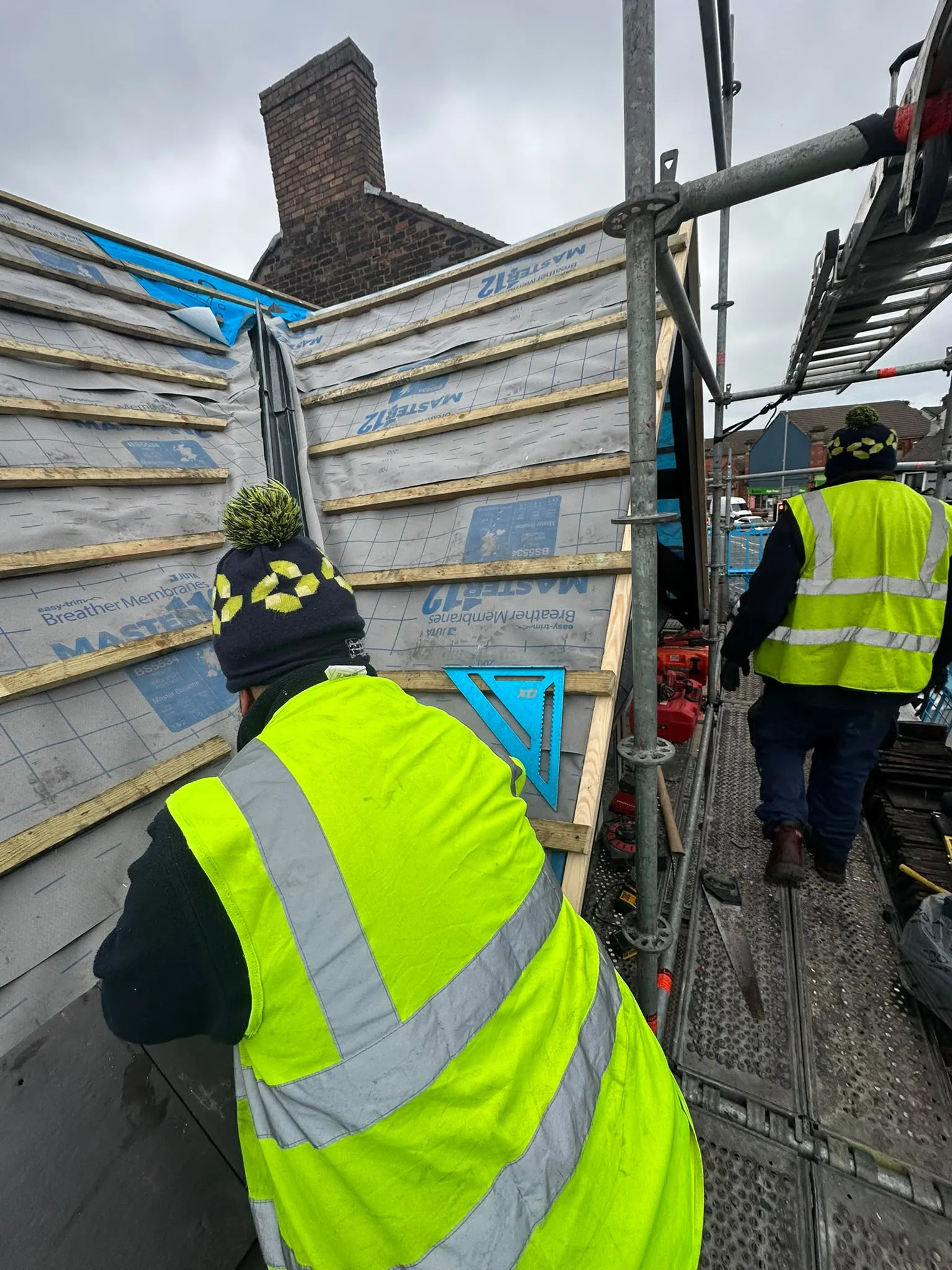 Roofers on scaffolding beside a roof covered in membrane and battens